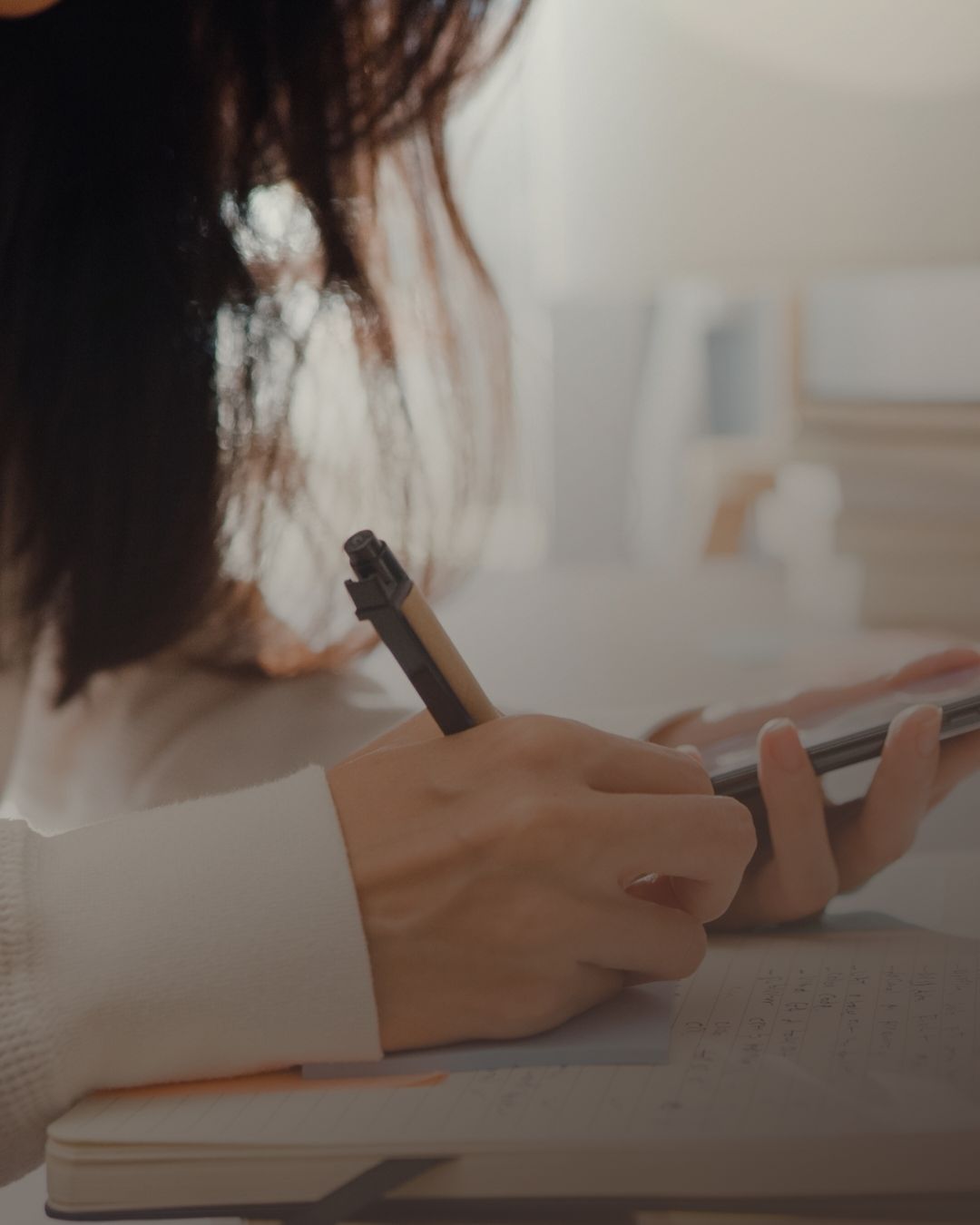 Vrouw schrijft met een pen in een notitieboek met haar telefoon in de andere hand